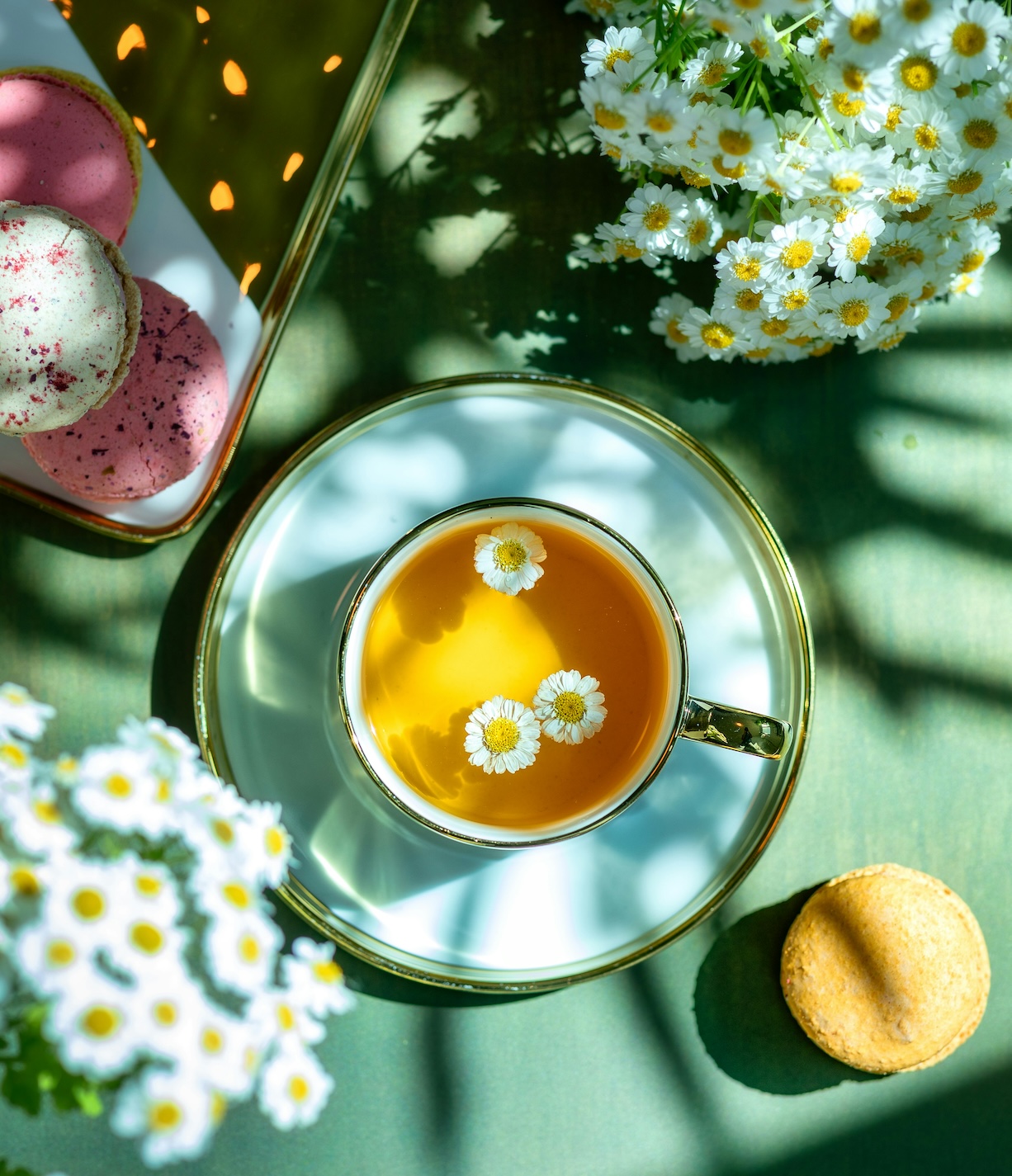 tea cup with flowers floating inside resting on a table next to macrons